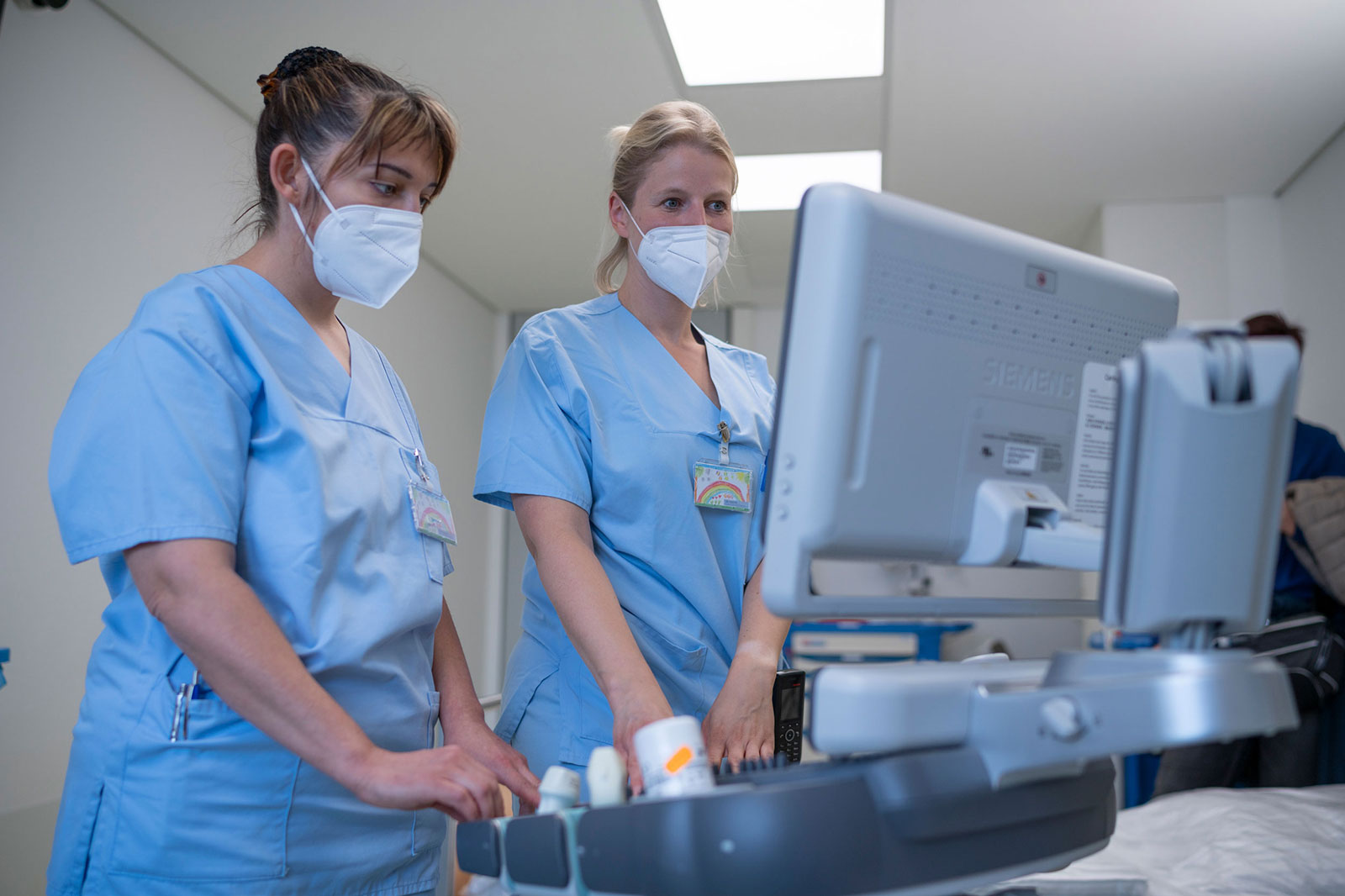 Auf einem Monitor kontrollieren zwei Pflegekräfte die Werte eines Patienten im Intensivbett.